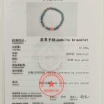 A certificate showing an image of the Green Jadeite Bracelet – Round Beads with Clear Buddha-Head Charm, including gemstone details, weight, shape, official seals, identification numbers, and other gemological information.