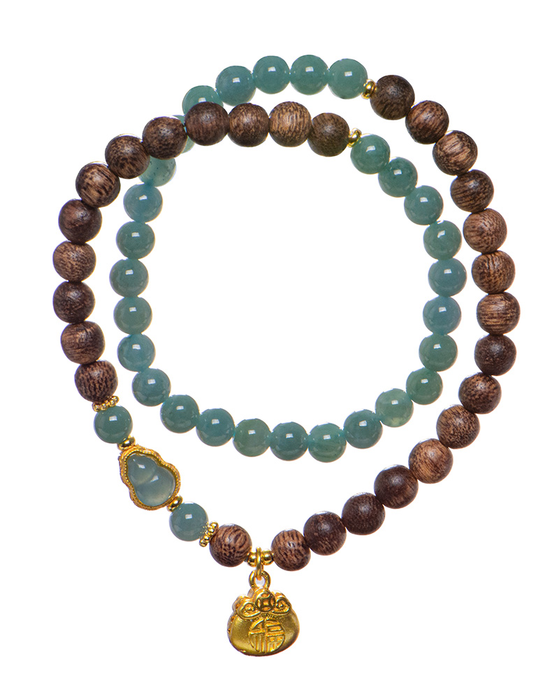 LYU_3788 The Sandalwood & Green Jadeite Double-Strand Bracelet features round green jadeite and brown sandalwood beads with gold accents, a pouch charm, and a decorative green stone. Both strands are coiled together on a white background.