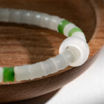 A close-up of the Natural white Nephrite Jade Bracelet – Handmade Beads Stretch Bracelet with frosted white and green beads, displayed on a smooth wooden dish in gentle natural light that highlights its textured beauty.