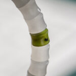 A close-up of the White with Purple Veining Nephrite Jade Bracelet—disc beads and Hetian Biyu accents—shows a translucent white bead with a green center and a small dark spot, set against a softly blurred white and teal background.