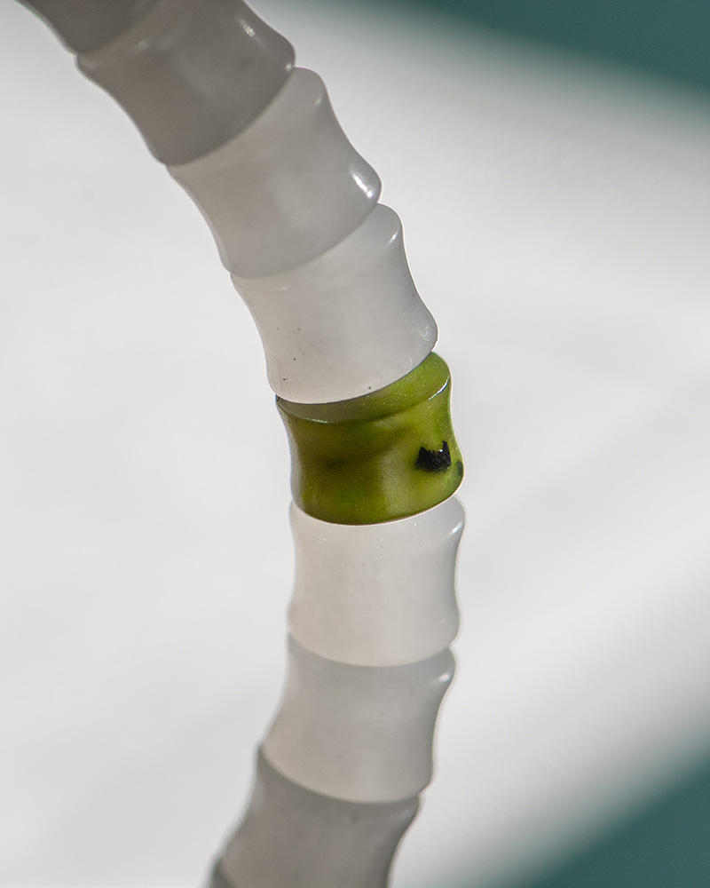 A close-up of the White with Purple Veining Nephrite Jade Bracelet—disc beads and Hetian Biyu accents—shows a translucent white bead with a green center and a small dark spot, set against a softly blurred white and teal background.