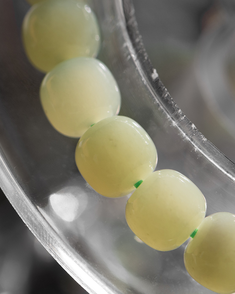 LYU_3919 Close-up of the Handmade Jade Bracelet featuring glossy, translucent pale yellow nephrite beads strung on green thread, resting on a clear plastic surface—an elegant natural stone jewelry gift for healing, balance, and good luck.