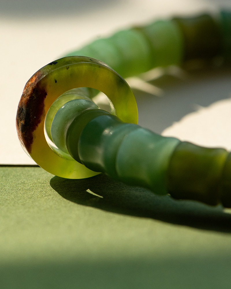 LYU_3939 Close-up of the Nephrite Jade Bead Bracelet – Unique Ring with Natural Jade Skin, resting on a surface with soft lighting that highlights the translucent green beads and their varied natural hues.