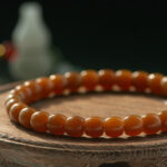 A close-up of the Natural Hetian Jade Beaded Bracelet for meditation and energy, resting on a wooden surface with a blurred white object in the background.