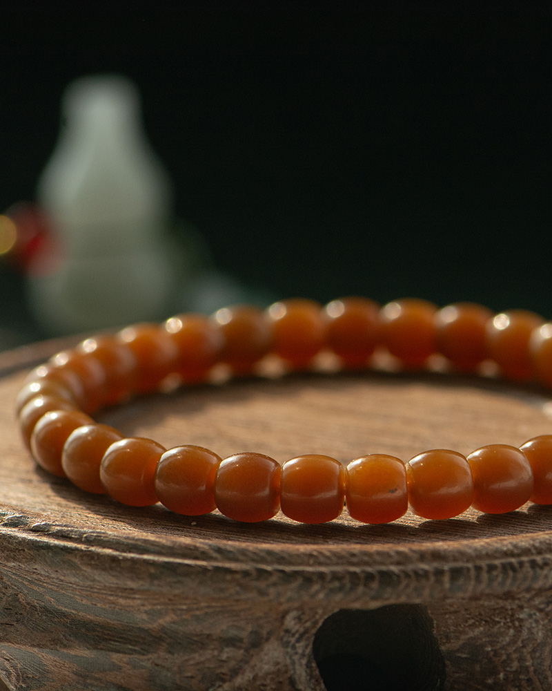 A close-up of the Natural Hetian Jade Beaded Bracelet for meditation and energy, resting on a wooden surface with a blurred white object in the background.