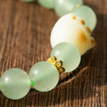 A close-up of the Mint Green Aventurine Quartz Bracelet featuring round, translucent beads and a cat paw charm, displayed on a wooden surface.