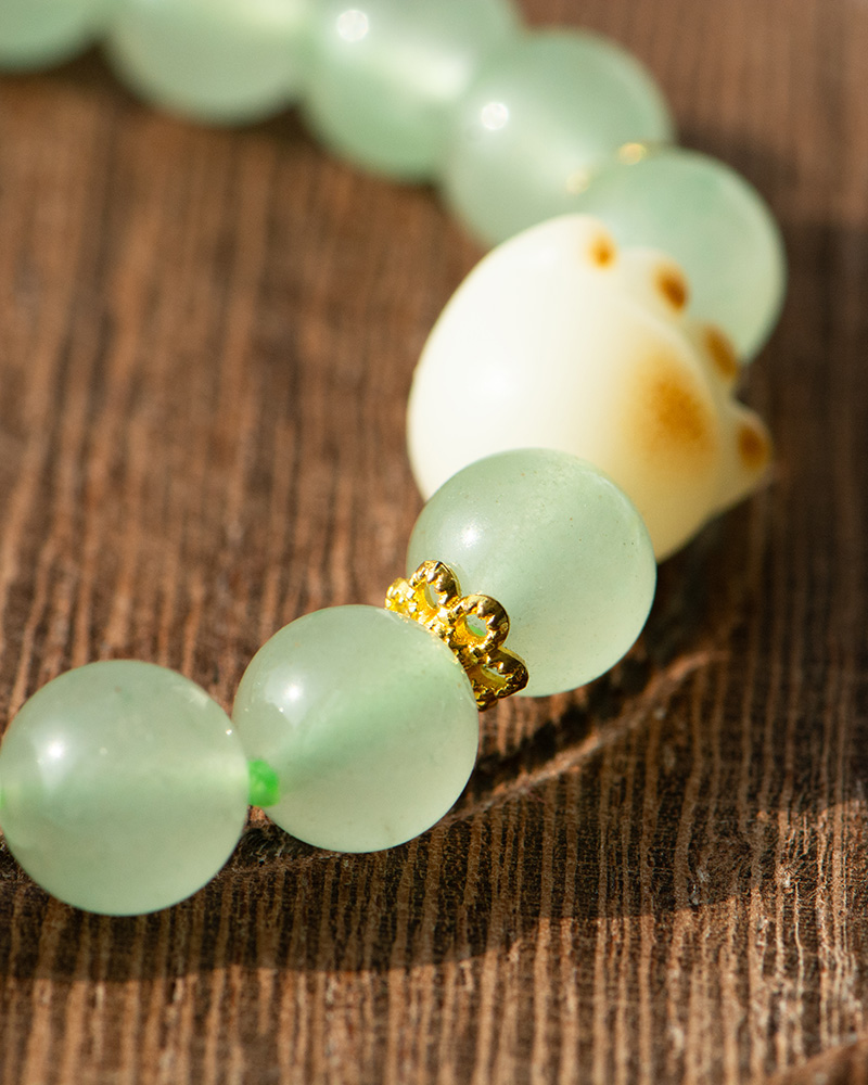 LYU_3954 A close-up of the Mint Green Aventurine Quartz Bracelet featuring round, translucent beads and a cat paw charm, displayed on a wooden surface.