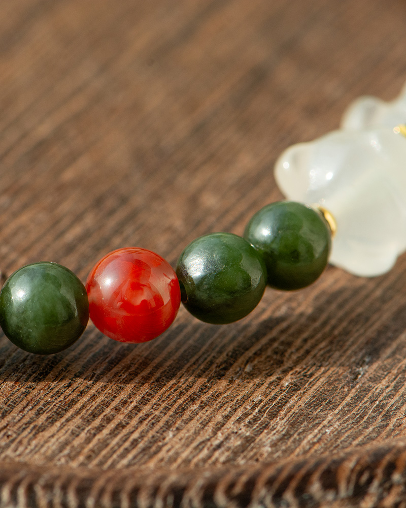 LYU_3964 A close-up of the Deep Green Nephrite Jade Bracelet, featuring round beads, a translucent red agate accent, and a white Yanyuan bear charm, displayed on textured wood.