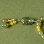 Olive Green Nephrite Jade Wrap Bracelet features round beads and a central carved green bead; can be worn as a convertible necklace, shown here on an olive-green background.