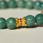 A close-up of the Green Jadeite Bracelet featuring round green beads and a clear Buddha-head charm at the center.