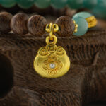 A close-up of the Sandalwood & Green Jadeite Double-Strand Bracelet, featuring round green jadeite and sandalwood beads with a gold-tone pouch charm, displayed on a textured wooden surface.