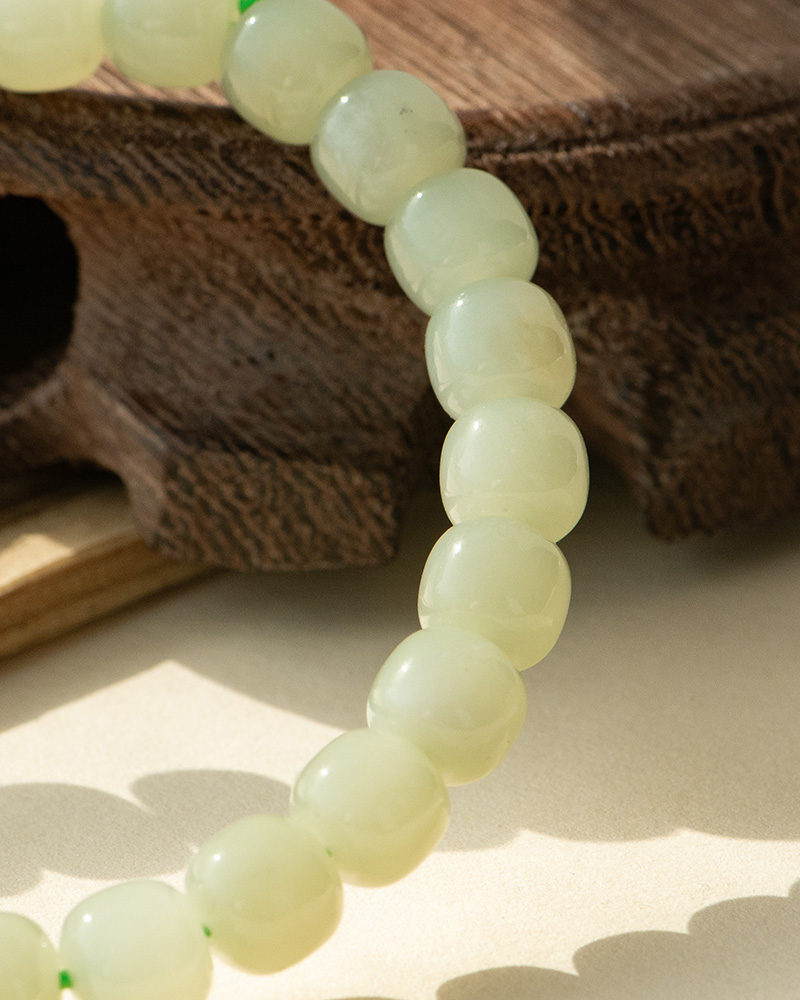 LYU_4018 A close-up of the Handmade Jade Bracelet, crafted from smooth, glossy pale green natural nephrite beads strung closely together, resting on wood with sunlight highlighting their texture—perfect for healing, balance, and good luck.