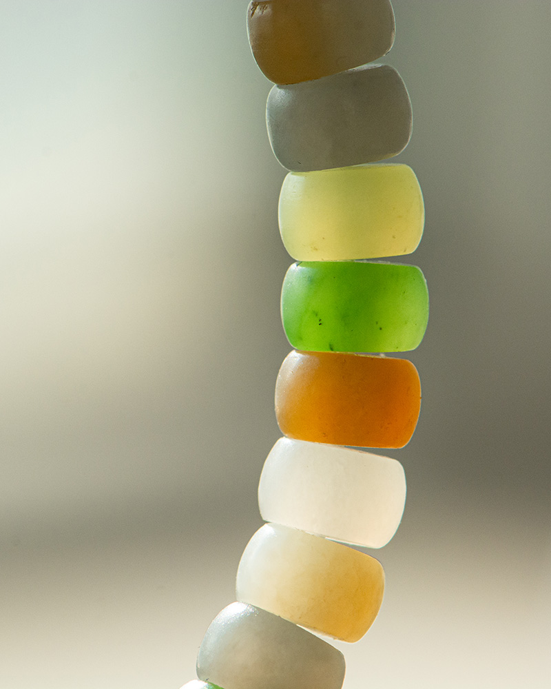 LYU_4045 A close-up of the Pastel Spectrum Nephrite Jade Bracelet – Heishi Rondelles, featuring translucent, rounded beads in white, yellow, green, and orange against a blurred neutral background.