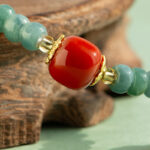 Close-up of the Teal Green Jadeite Bracelet, showcasing disc beads with trio charms and a polished centerpiece, accented by gold details and resting on a wooden surface.