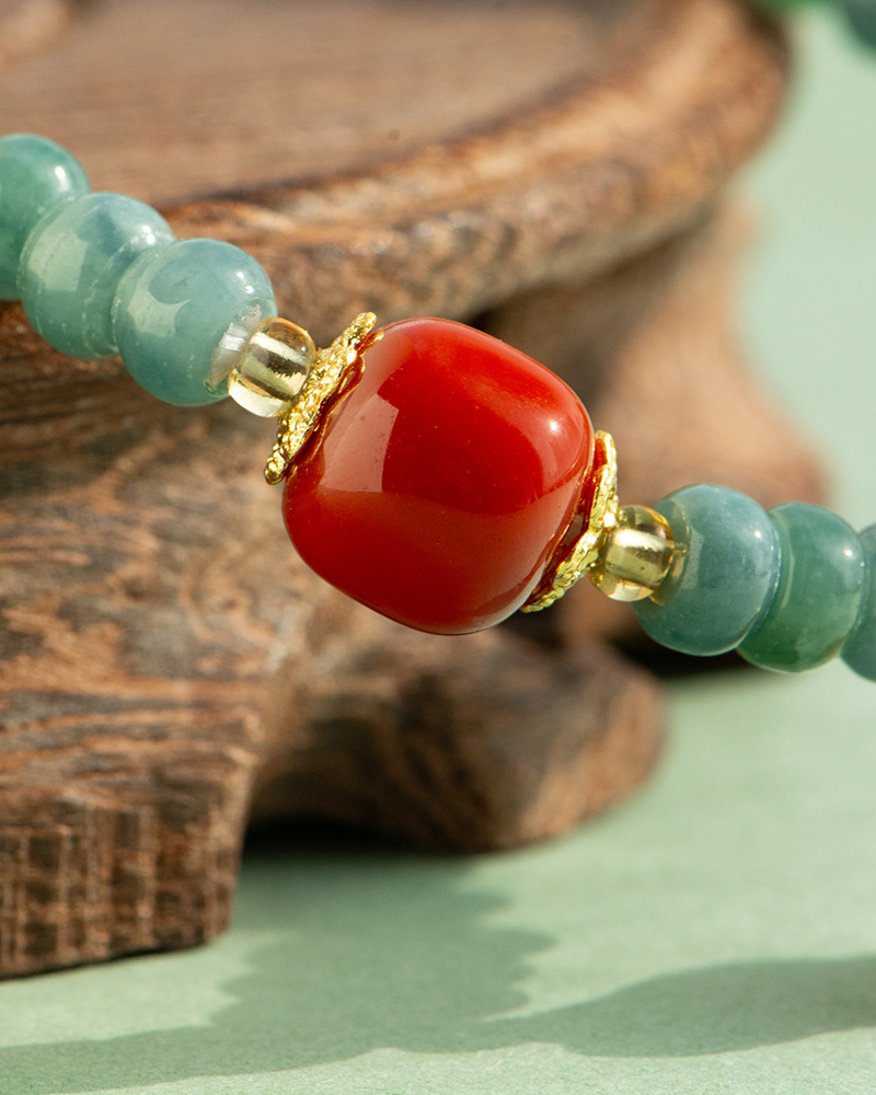 LYU_4056 Close-up of the Teal Green Jadeite Bracelet, showcasing disc beads with trio charms and a polished centerpiece, accented by gold details and resting on a wooden surface.
