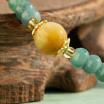 A close-up of the Teal Green Jadeite Bracelet—featuring disc beads and trio charms—resting on a wooden surface.