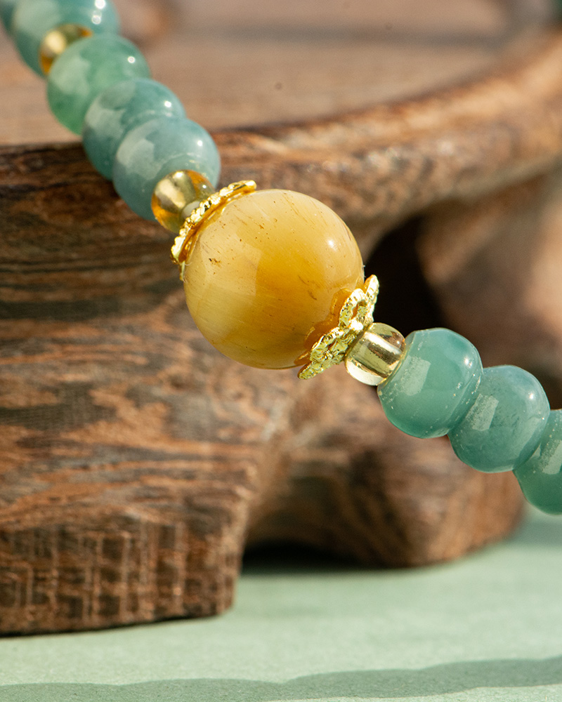 LYU_4059 A close-up of the Teal Green Jadeite Bracelet—featuring disc beads and trio charms—resting on a wooden surface.