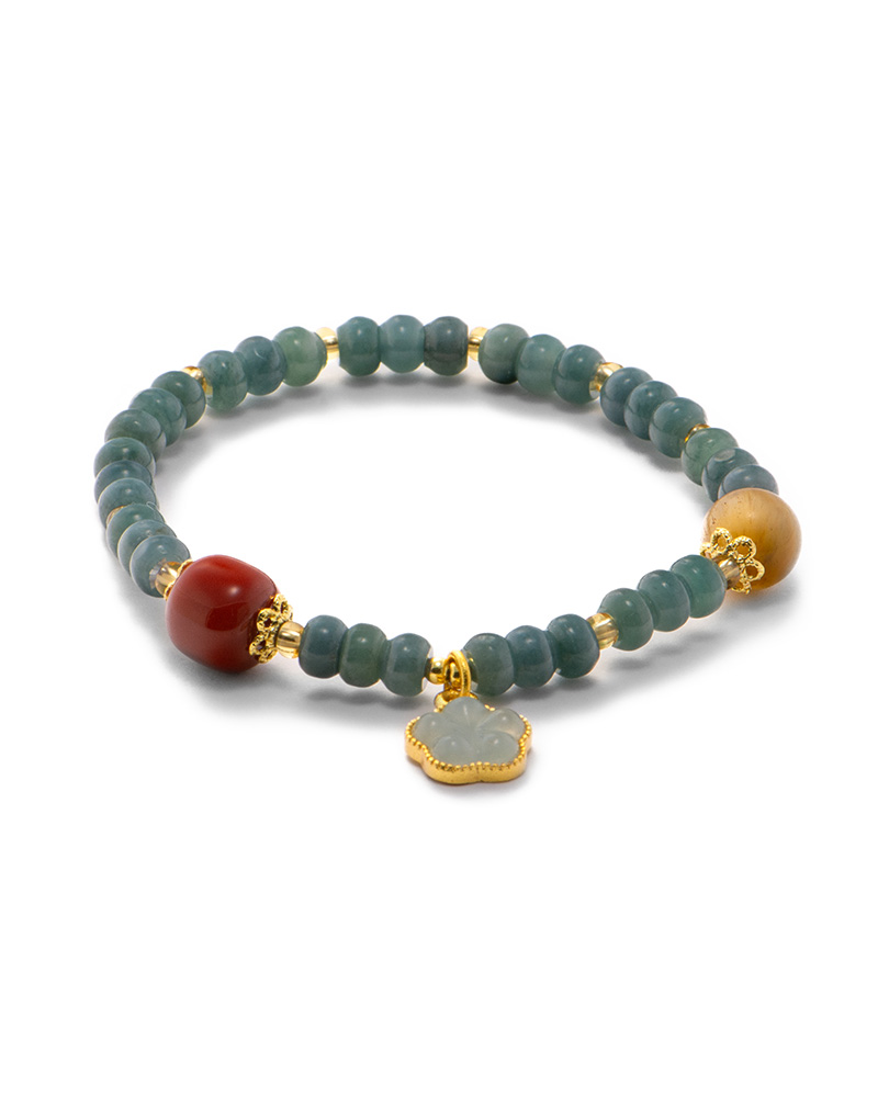 LYU_4081 Studio photo of a deep green Jadeite bracelet, featuring disc beads with gold-tone spacers and a carved floral charm, on a white background.