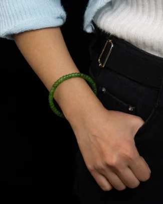 Wearing the Fresh Green Nephrite Jade Bracelet – Slim Rondelle Beads, Clean Minimal Strand, a person rests their hand on the pocket of black jeans, with a blue sweater sleeve partially visible.