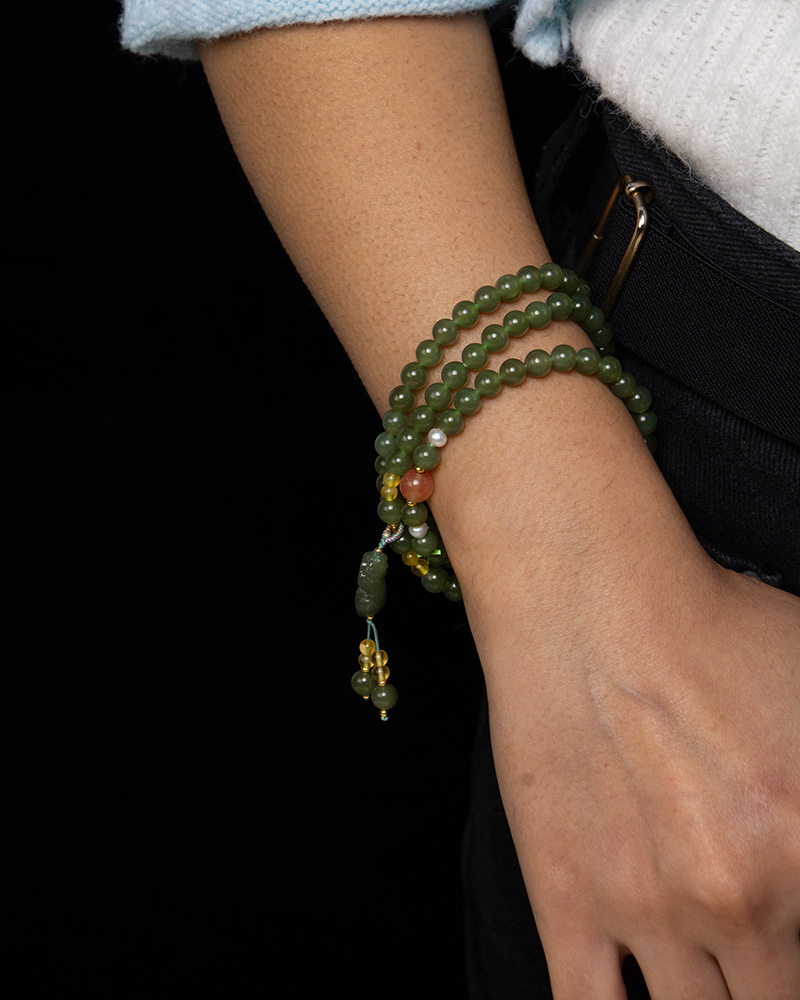 LYU_4239 Someone wearing the Olive Green Nephrite Jade Wrap Bracelet – a stylish accessory with round beads that can also be worn as a convertible necklace.