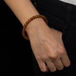 A person in dark pants and a white top has their right hand in their pocket, showcasing the Natural Hetian Jade Beaded Bracelet – Beads for Meditation & Energy on their wrist against a black background.