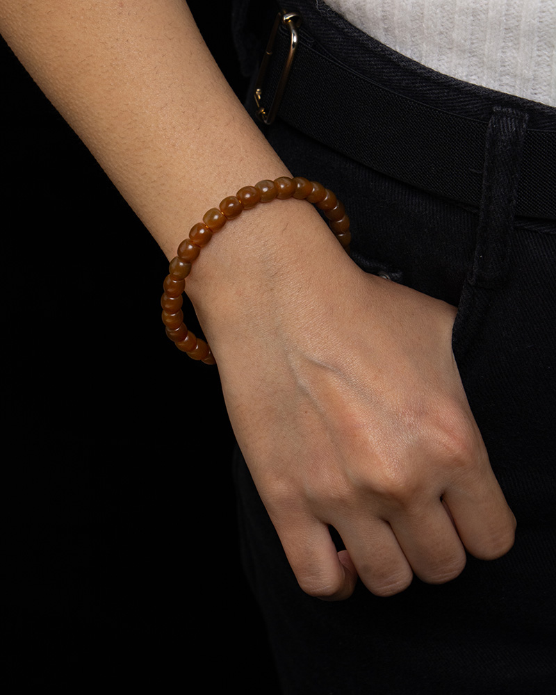 A person in dark pants and a white top has their right hand in their pocket, showcasing the Natural Hetian Jade Beaded Bracelet – Beads for Meditation & Energy on their wrist against a black background.