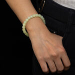 A person in a white shirt and dark pants slips a hand into their pocket, displaying the Handmade Jade Bracelet – Natural Nephrite Stone Jewelry Gift for Healing, Balance, and Good Luck on their wrist.