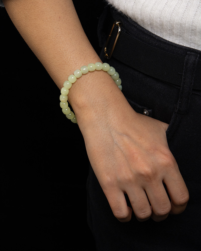 LYU_4246 A person in a white shirt and dark pants slips a hand into their pocket, displaying the Handmade Jade Bracelet – Natural Nephrite Stone Jewelry Gift for Healing, Balance, and Good Luck on their wrist.