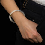 A person in a white sweater and black pants, with their hand in their pocket, displays a White with Purple Veining Nephrite Jade Bracelet – Disc Beads with Hetian Biyu Accents on their wrist.