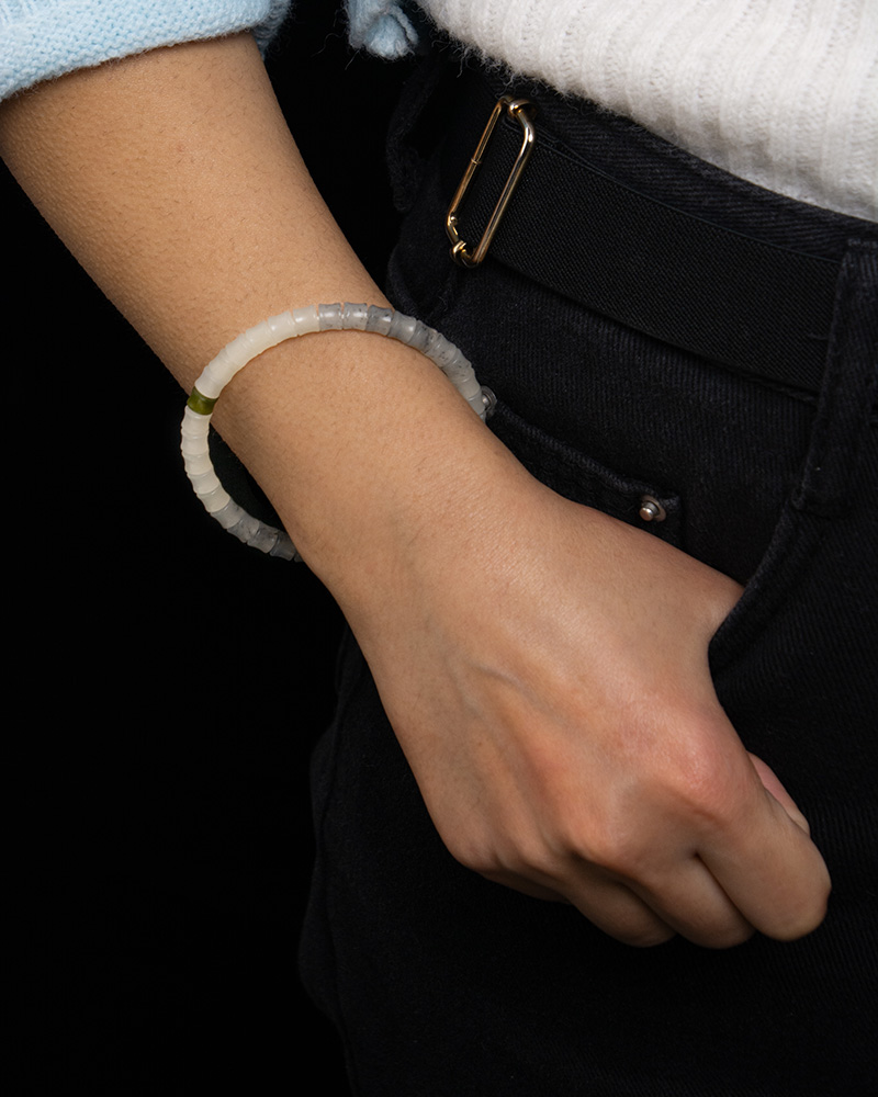 A person in a white sweater and black pants, with their hand in their pocket, displays a White with Purple Veining Nephrite Jade Bracelet – Disc Beads with Hetian Biyu Accents on their wrist.