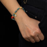 A person wearing black pants with a hand in the pocket, showcasing the Teal Green Jadeite Bracelet – Disc Beads with Trio Charms on their wrist.