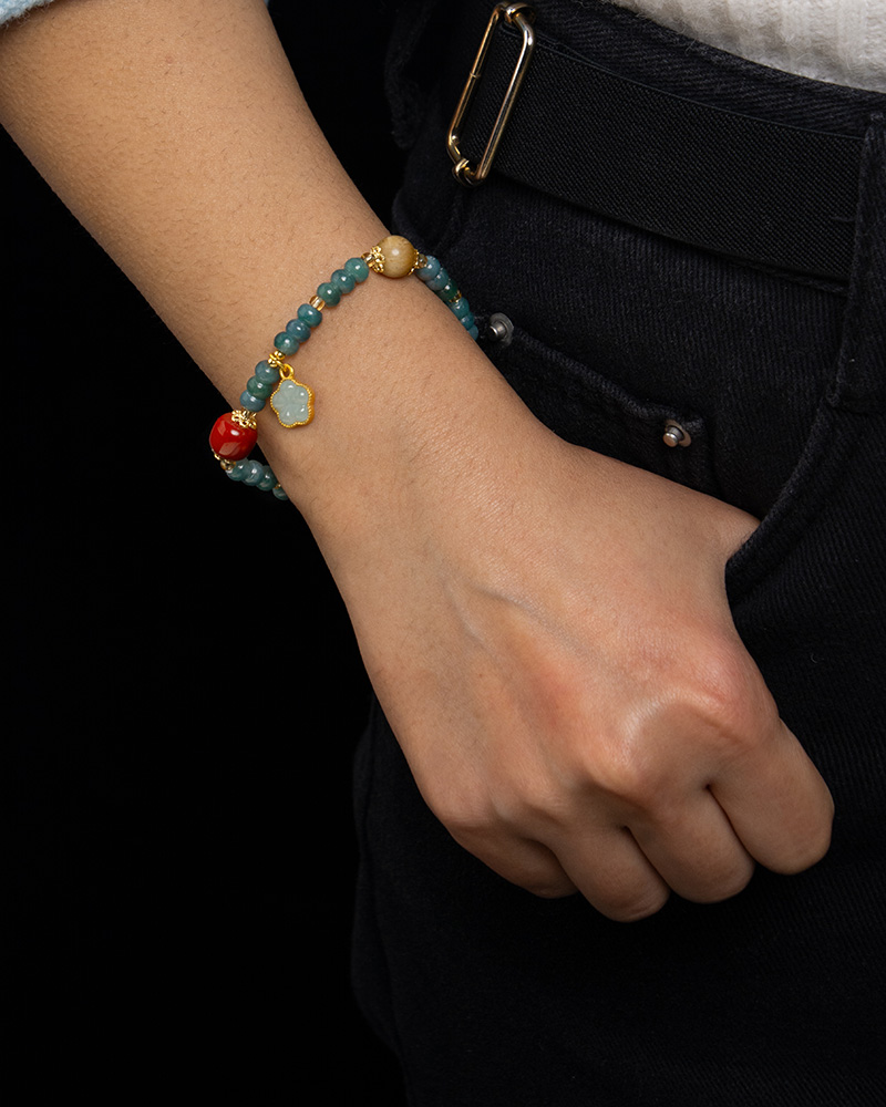 LYU_4255 A person wearing black pants with a hand in the pocket, showcasing the Teal Green Jadeite Bracelet – Disc Beads with Trio Charms on their wrist.