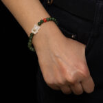 Someone wearing the Deep Green Nephrite Jade Bracelet, featuring round beads, red agate accents, and a Yanyuan bear charm, rests their hand near the pocket of dark pants.