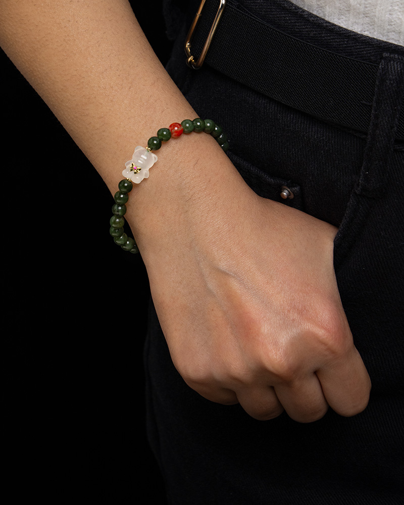 LYU_4256 Someone wearing the Deep Green Nephrite Jade Bracelet, featuring round beads, red agate accents, and a Yanyuan bear charm, rests their hand near the pocket of dark pants.
