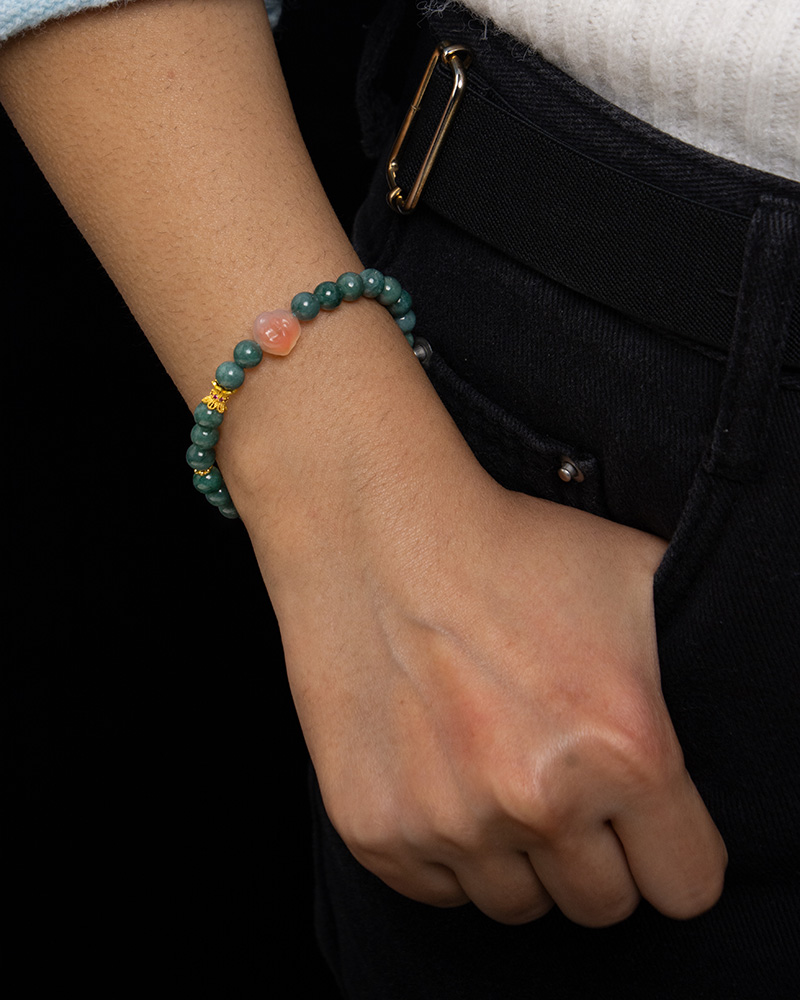LYU_4257 A person in black pants and a white top has their right hand in their pocket, showcasing the Green Jadeite Bracelet – round beads with a clear Buddha-head charm.