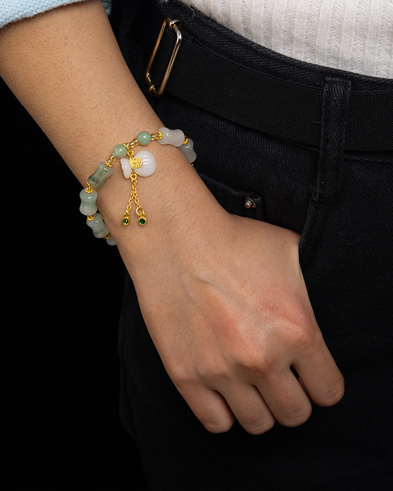 LYU_4259 A person wears the Icy Green Tianshan Cui Chalcedony Bracelet, featuring bamboo-knot beads and a white lucky pouch charm, with their hand resting on dark pants and paired with a light knit top.