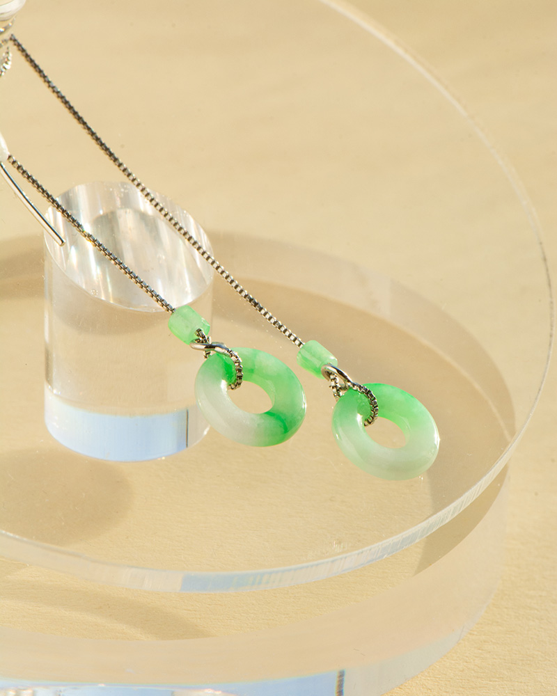 Greenish-White Jadeite Donut Threader Earrings in sterling silver are displayed on a clear, round acrylic stand against a beige background.