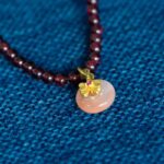 A close-up of the Wine-Red Garnet Wrap Bracelet, featuring round dark red beads and a persimmon charm pendant, displayed on textured blue fabric.