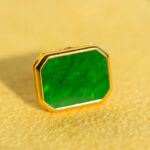 A close-up of Vivid Green Jadeite Stud Earrings featuring rectangular flat inlays in gold-plated 925 sterling silver, resting on a soft yellow surface.