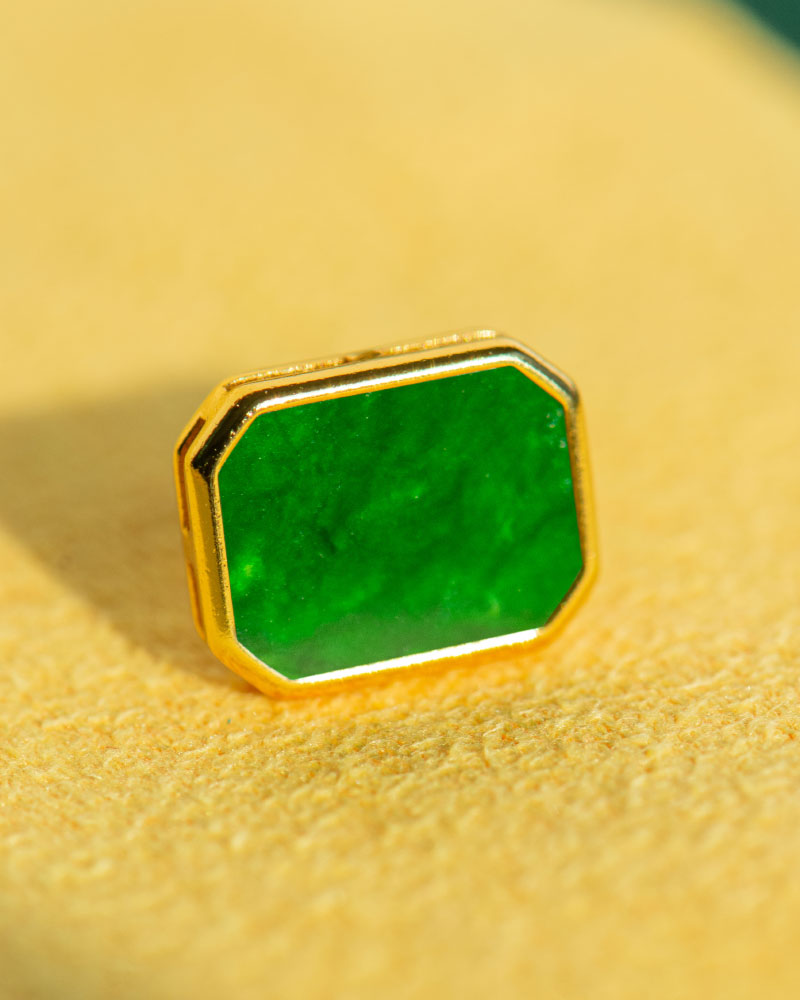 A close-up of Vivid Green Jadeite Stud Earrings featuring rectangular flat inlays in gold-plated 925 sterling silver, resting on a soft yellow surface.
