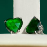Vivid Green Jadeite Stud Earrings feature heart-cut stones with custom faceting, set in 925 sterling silver prongs, displayed against a white and green background.