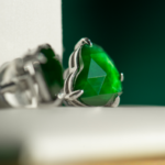Close-up of Vivid Green Jadeite Stud Earrings, heart-cut with custom faceting, set in 925 sterling silver, shown against a blurred white and green background.