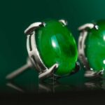 Close-up of a Vivid Green Jadeite Stud Earring, featuring a round cabochon set in 925 sterling silver. The polished jadeite's glossy surface is accentuated by a matching green background, highlighting its vibrant color.