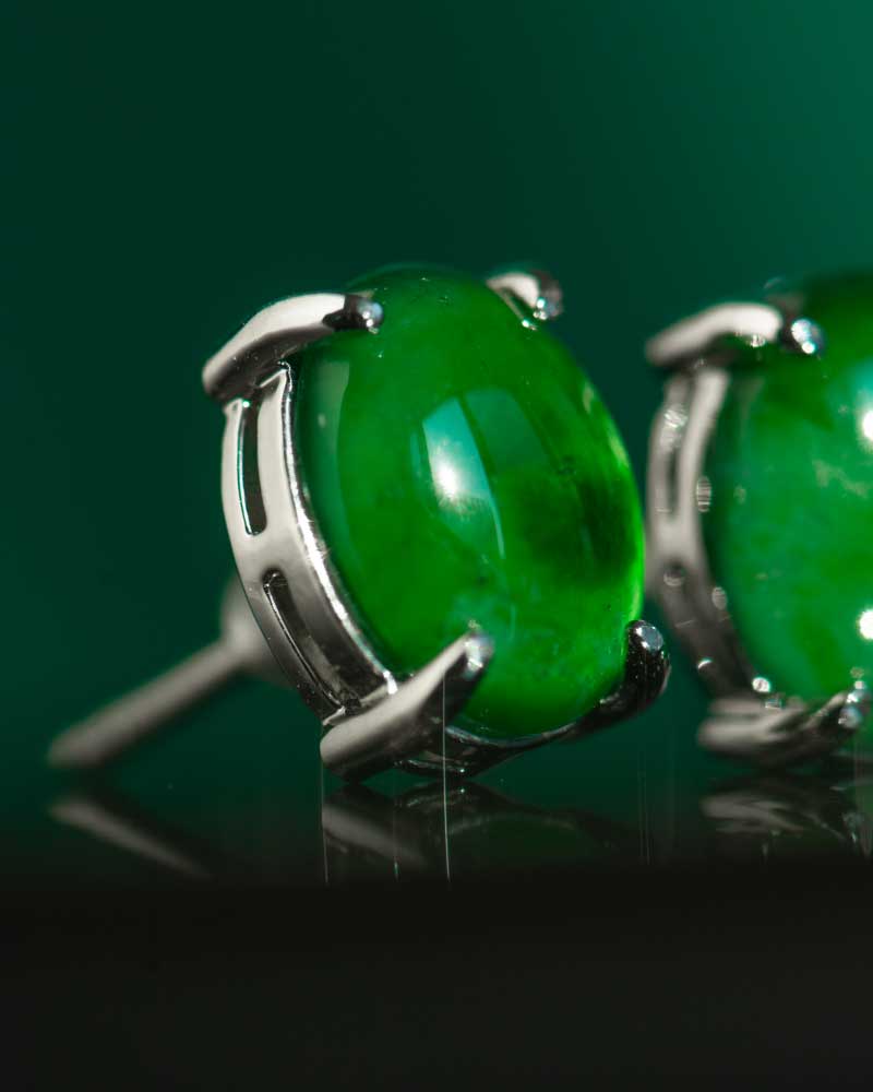Close-up of a Vivid Green Jadeite Stud Earring, featuring a round cabochon set in 925 sterling silver. The polished jadeite's glossy surface is accentuated by a matching green background, highlighting its vibrant color.