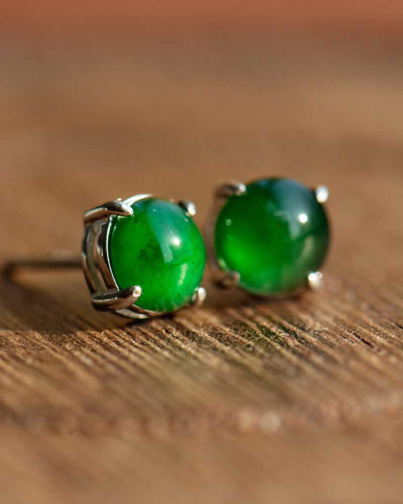 LYU_4963 A close-up of the Vivid Green Jadeite Stud Earrings, showcasing round cabochon beads in a silver setting, displayed on a wooden surface.