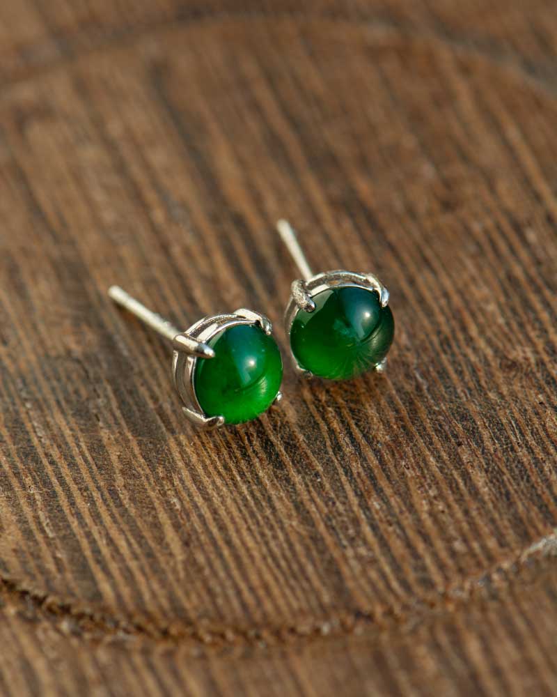 LYU_4965 Vivid Green Jadeite Stud Earrings feature round cabochon beads set in silver, showcased on a textured wooden surface.