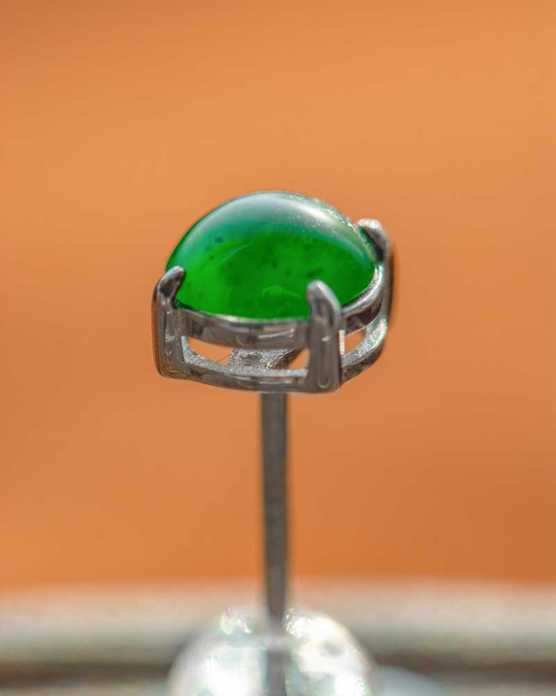 LYU_4966 A close-up of Vivid Green Jadeite Stud Earrings featuring round cabochon beads in a silver setting, with a blurred orange background.