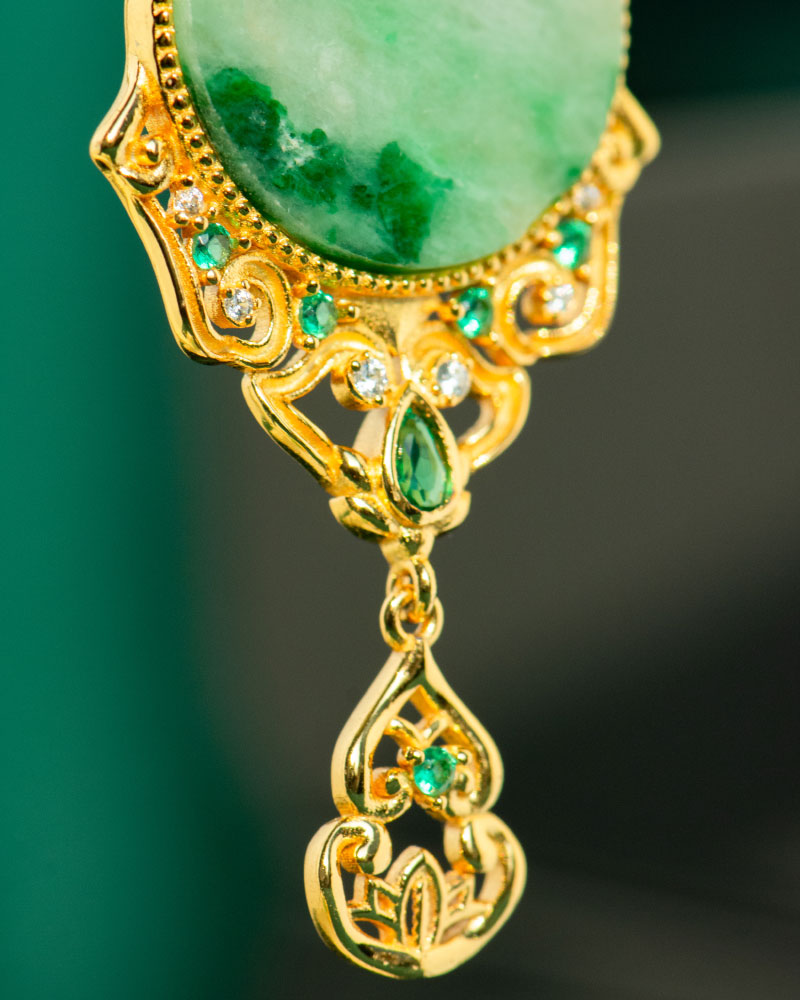 Close-up of the Jadeite Drop Earring—Chinese-inspired filigree in gold-plated 925 sterling silver, with a large green jade stone, accented by small green and white gemstones and a decorative dangling gold element.