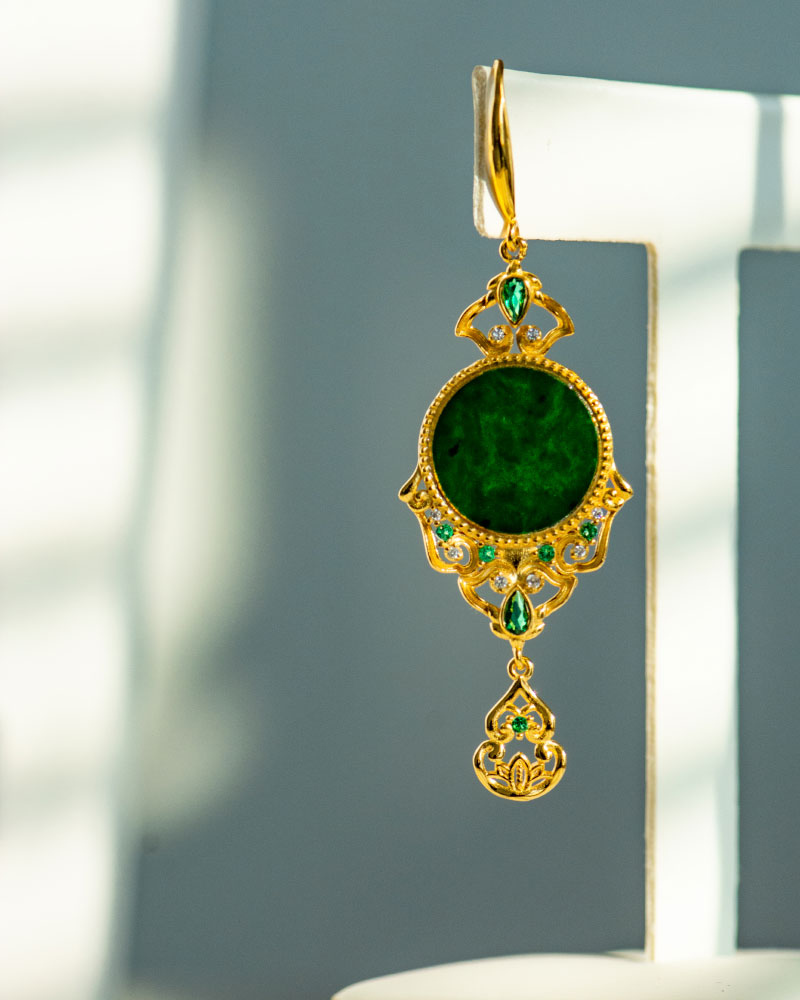 LYU_4977 The Deep Green Jadeite Drop Earring features gold-plated 925 silver with Chinese-inspired filigree, a large round jadeite center, small green gems, and hangs against a softly lit backdrop.