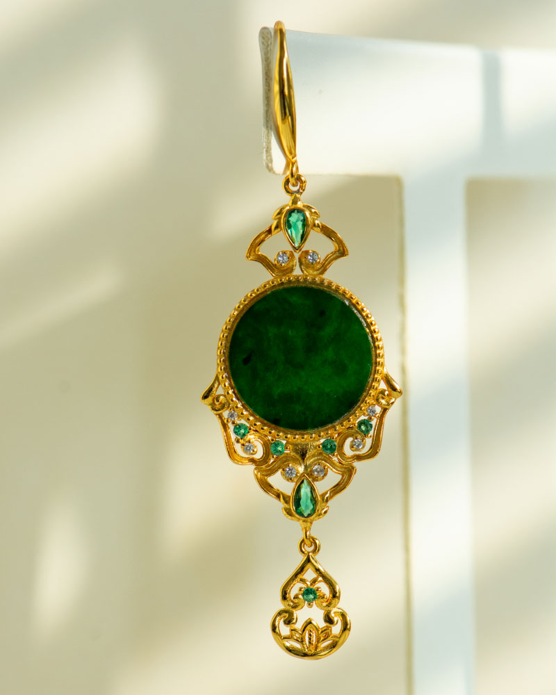 LYU_4978 The Deep Green Jadeite Drop Earring features Chinese-inspired filigree in gold-plated 925 sterling silver, with a large round green jadeite center, smaller gemstones, and a dangling design against a light background.